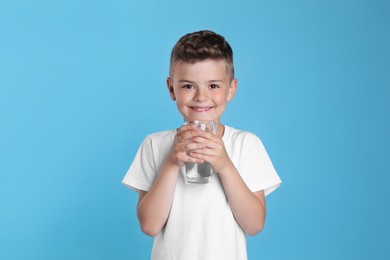 Photo of Cute little boy with glass of water on light blue background