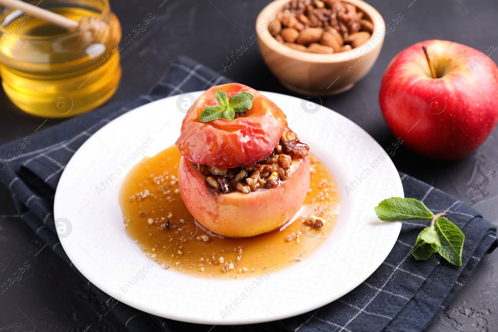 Photo of Tasty baked apple with nuts, honey and mint on gray table