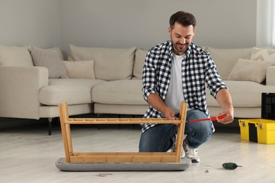 Photo of Man assembling shoe storage bench with screwdriver on floor at home
