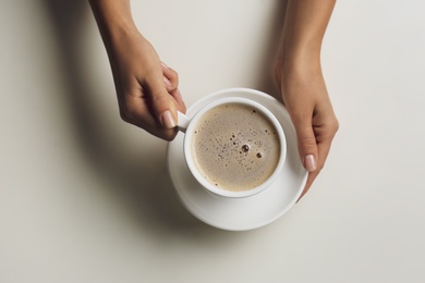 Photo of Woman holding cup of coffee at white table, top view