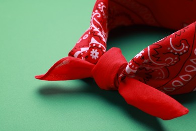Tied red bandana with paisley pattern on light green background, closeup