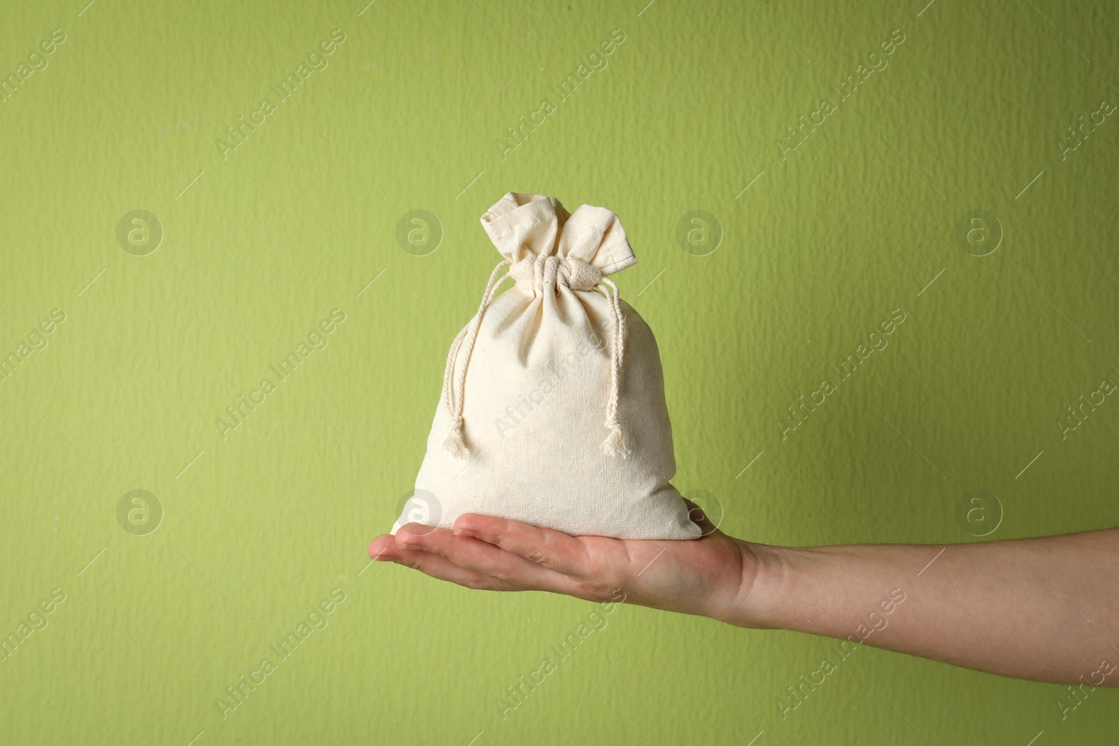 Photo of Woman holding full cotton eco bag on light green background, closeup