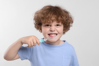 Cute little boy brushing his teeth with electric toothbrush on white background