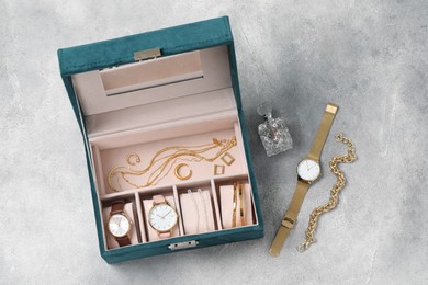 Photo of Jewelry box with many different accessories and perfume on light grey table, flat lay