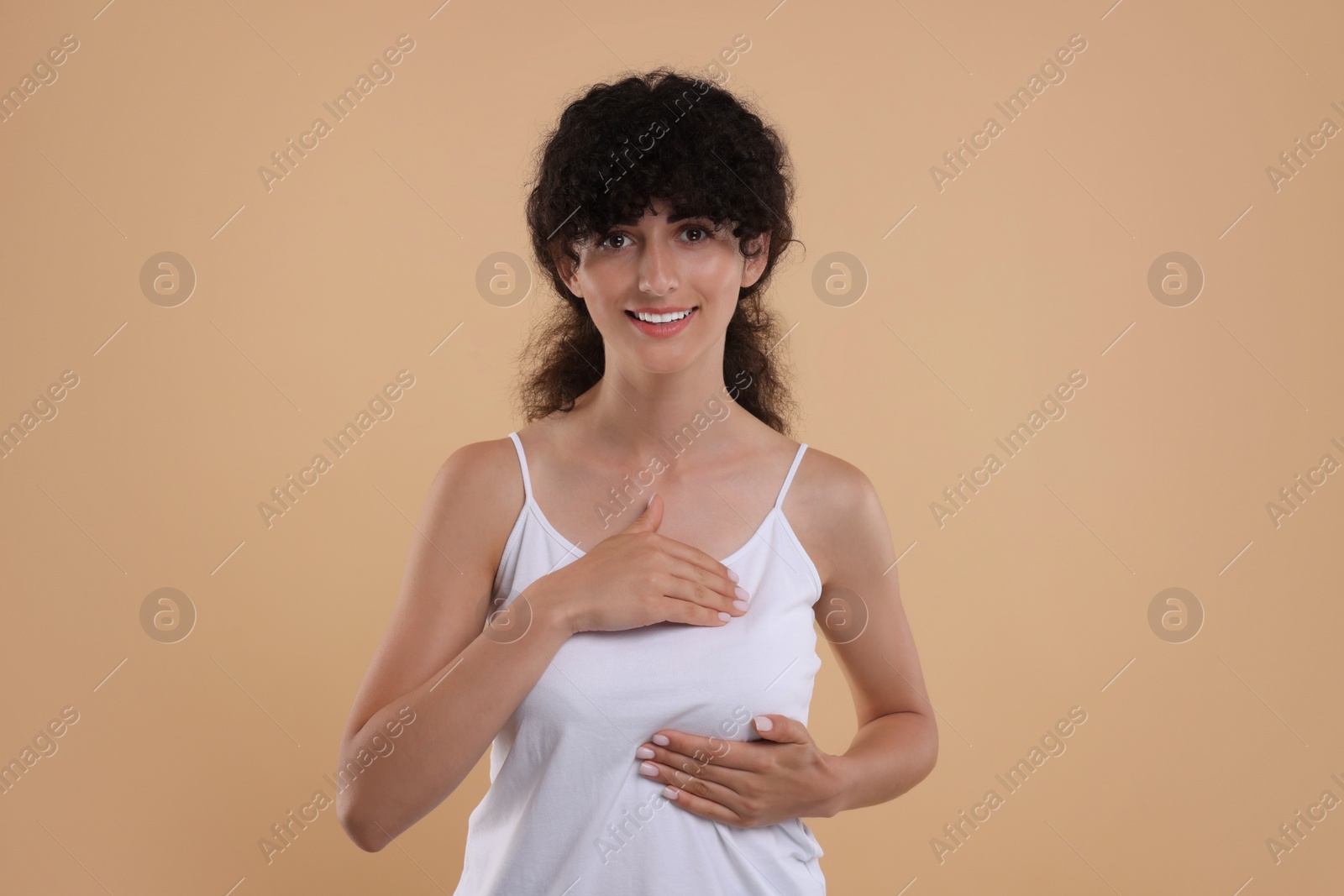 Photo of Smiling young woman doing breast self-examination on light brown background