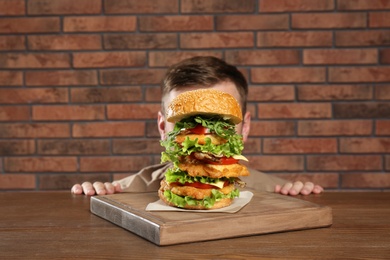 Photo of Man hiding behind huge burger on table