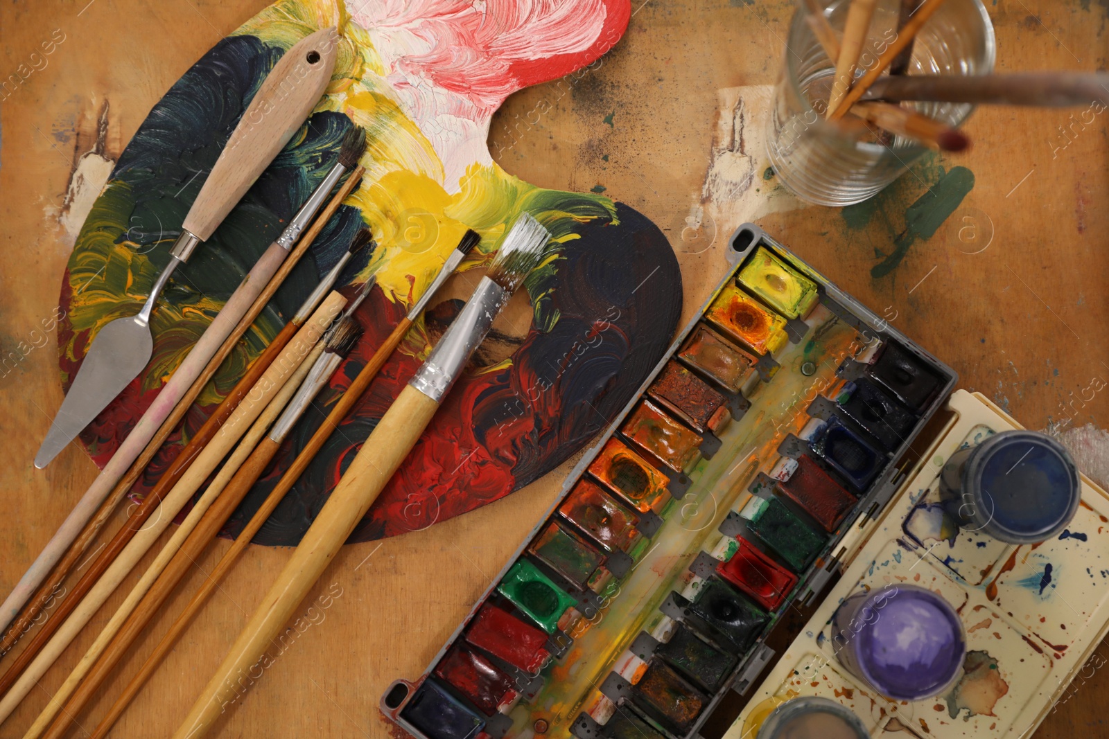 Photo of Spatula, brushes and paints on wooden table, flat lay