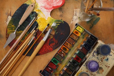 Photo of Spatula, brushes and paints on wooden table, flat lay