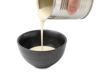 Photo of Woman pouring condensed milk from tin can into bowl isolated on white, closeup