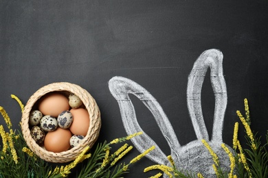 Photo of Easter bunny ears drawing and basket with eggs on blackboard, top view