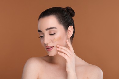 Woman with swatch of foundation on face against brown background