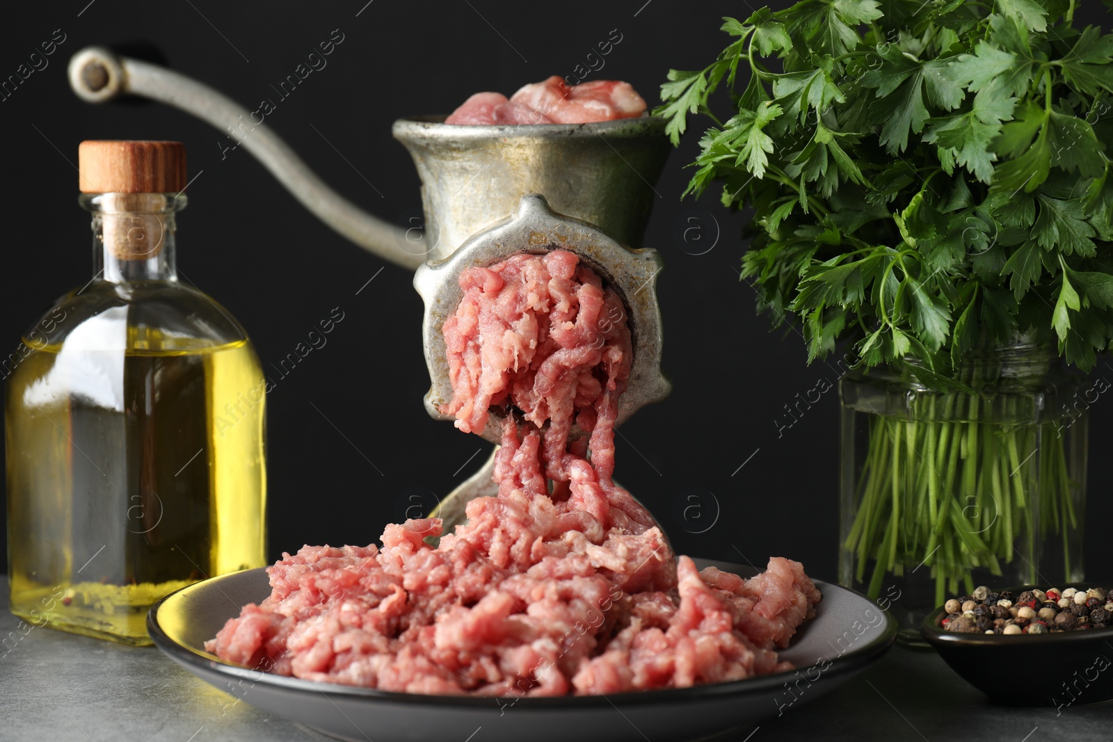 Photo of Manual meat grinder with beef mince, spices, oil and parsley on grey table