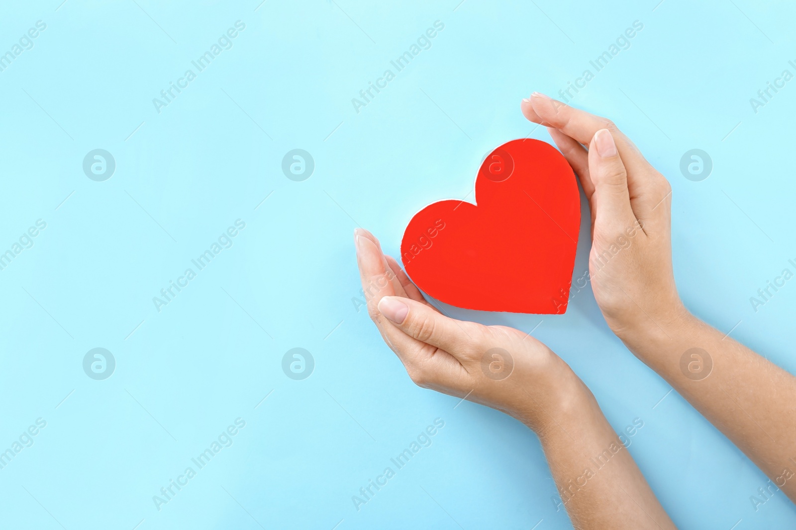 Photo of Woman holding hands near red heart on color background, top view