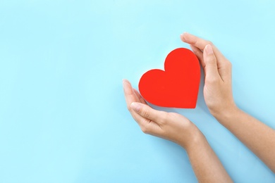 Woman holding hands near red heart on color background, top view