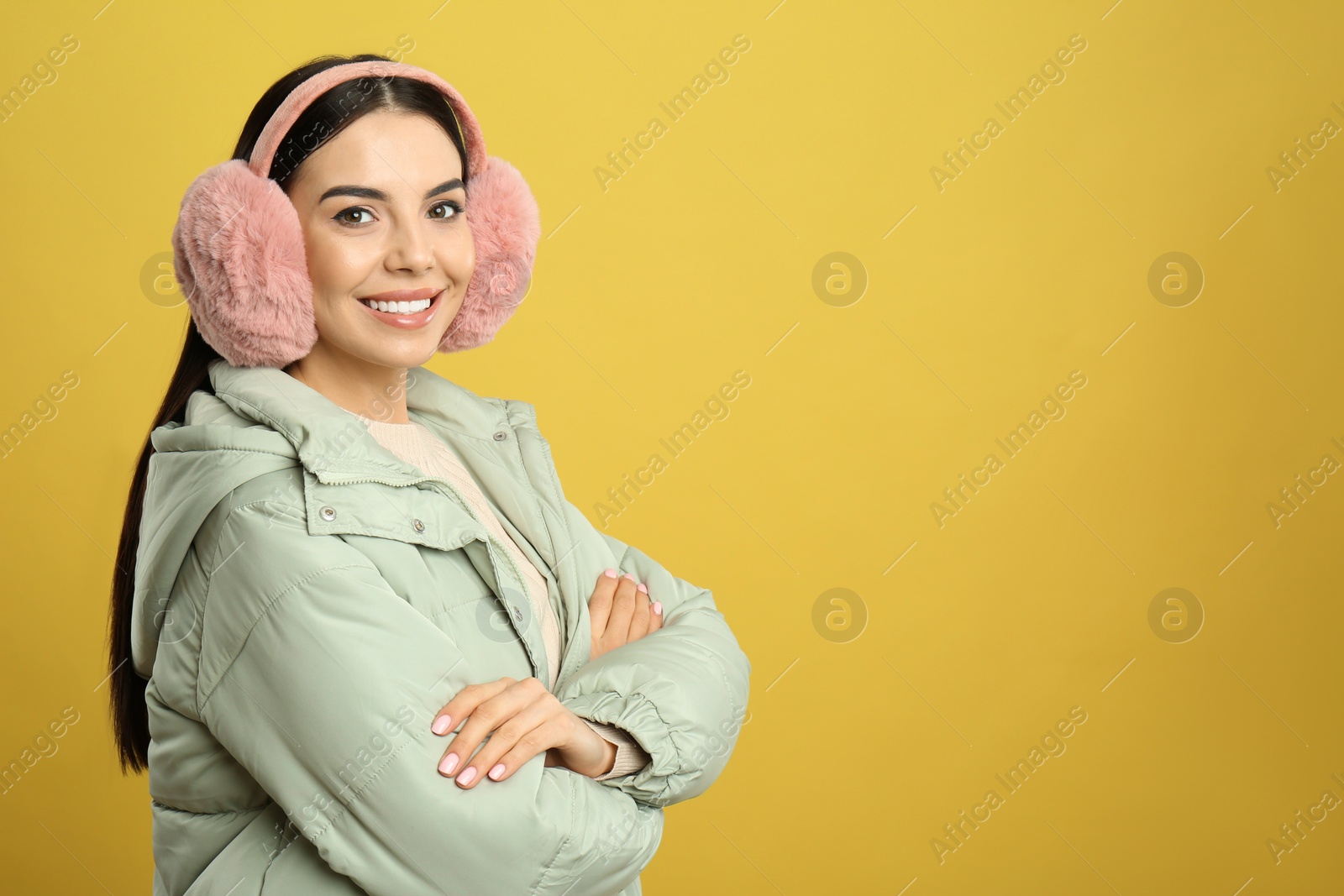 Photo of Beautiful young woman wearing earmuffs on yellow background. Space for text