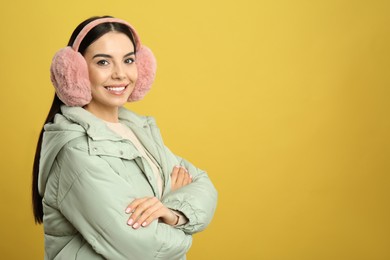 Photo of Beautiful young woman wearing earmuffs on yellow background. Space for text