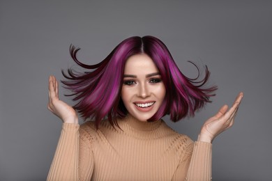 Hair styling. Attractive woman with bright purple hair on grey background