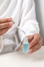 Photo of Woman with cosmetic serum at white table, closeup