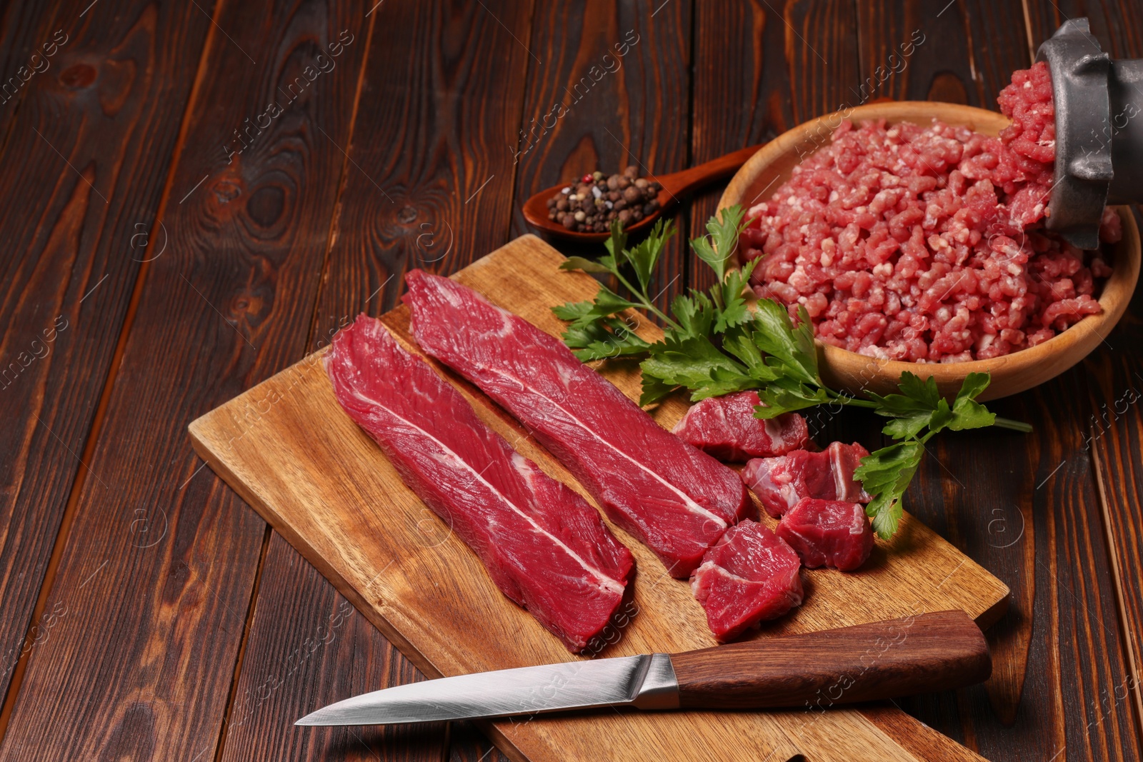 Photo of Manual meat grinder with beef, parsley and peppercorns on wooden table