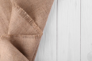 Photo of Brown burlap fabric on white wooden table, top view. Space for text
