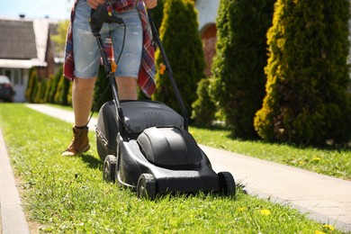 Photo of Man cutting green grass with lawn mower on backyard, closeup