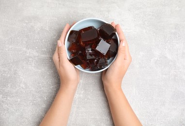 Photo of Woman holding bowl with delicious grass jelly cubes at light grey table, top view