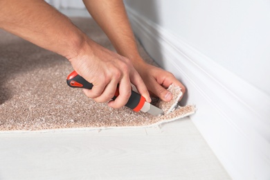 Man cutting new carpet flooring indoors, closeup