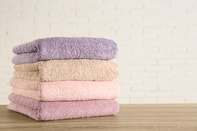 Photo of Stack of clean bath towels on wooden table near white brick wall. Space for text