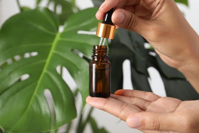 Woman with bottle of cosmetic serum near green plant, closeup. Space for text