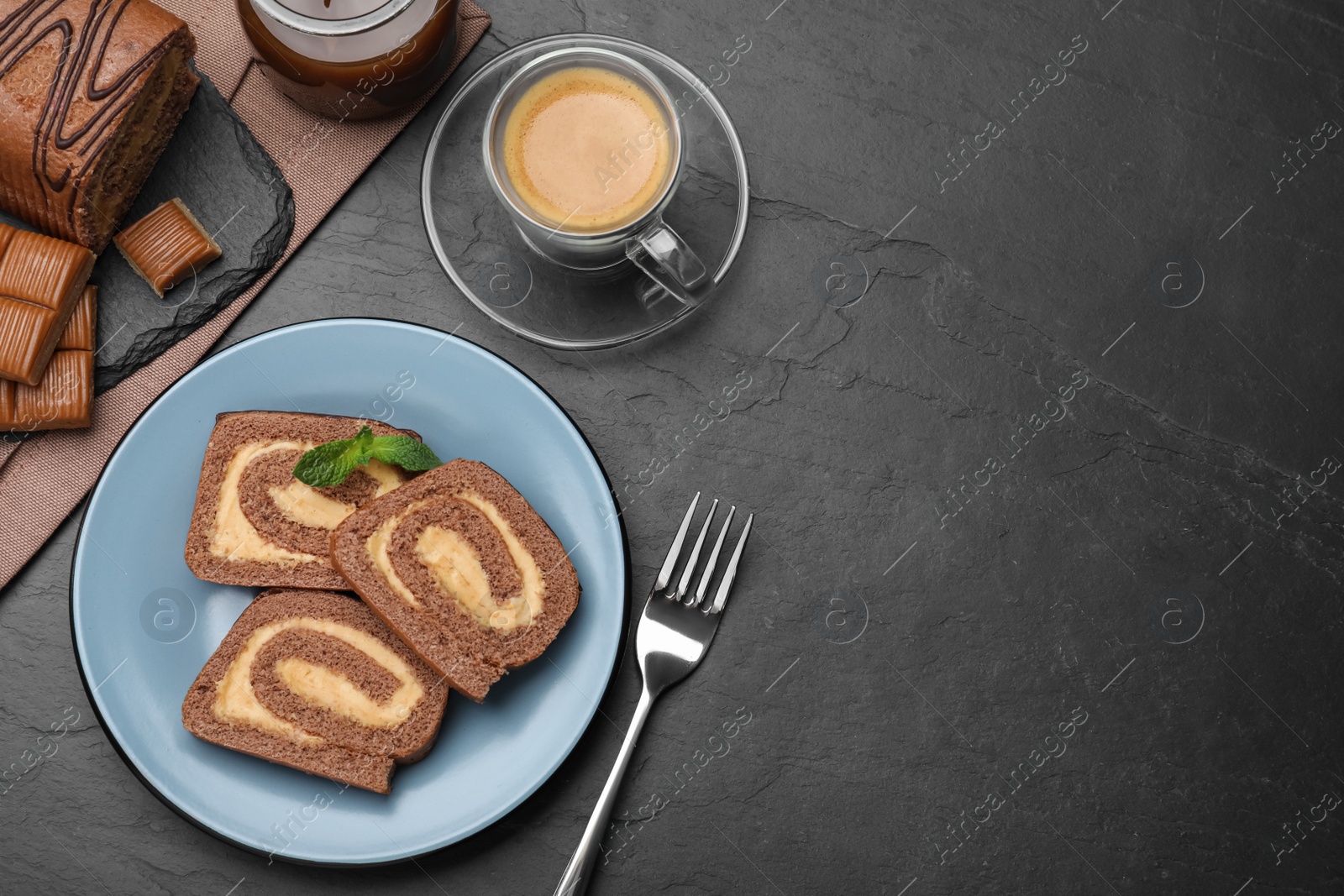 Photo of Tasty chocolate cake roll with cream and coffee on black table, flat lay. Space for text