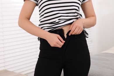 Photo of Woman trying to fit into her black jeans at home, closeup