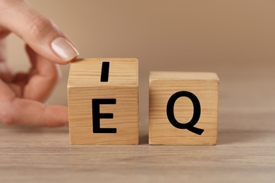 Photo of Woman turning cube with letters E and I near Q at wooden table, closeup