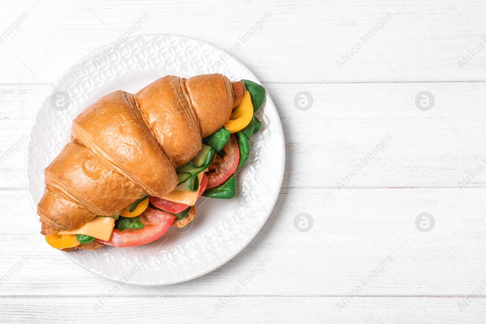 Photo of Tasty vegetarian croissant sandwich on white wooden table, top view. Space for text