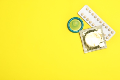 Condoms and birth control pills on yellow background, flat lay with space for text. Safe sex concept