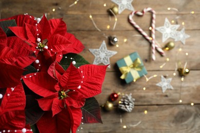 Photo of Poinsettia (traditional Christmas flower) with elegant bead garland and holiday items on wooden table, top view. Space for text