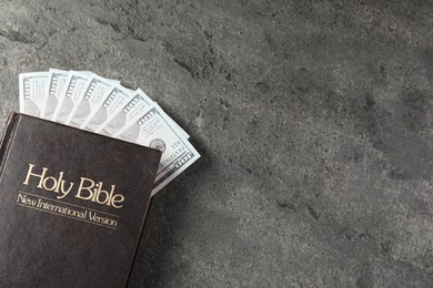 Photo of Holy Bible and money on grey table, top view. Space for text