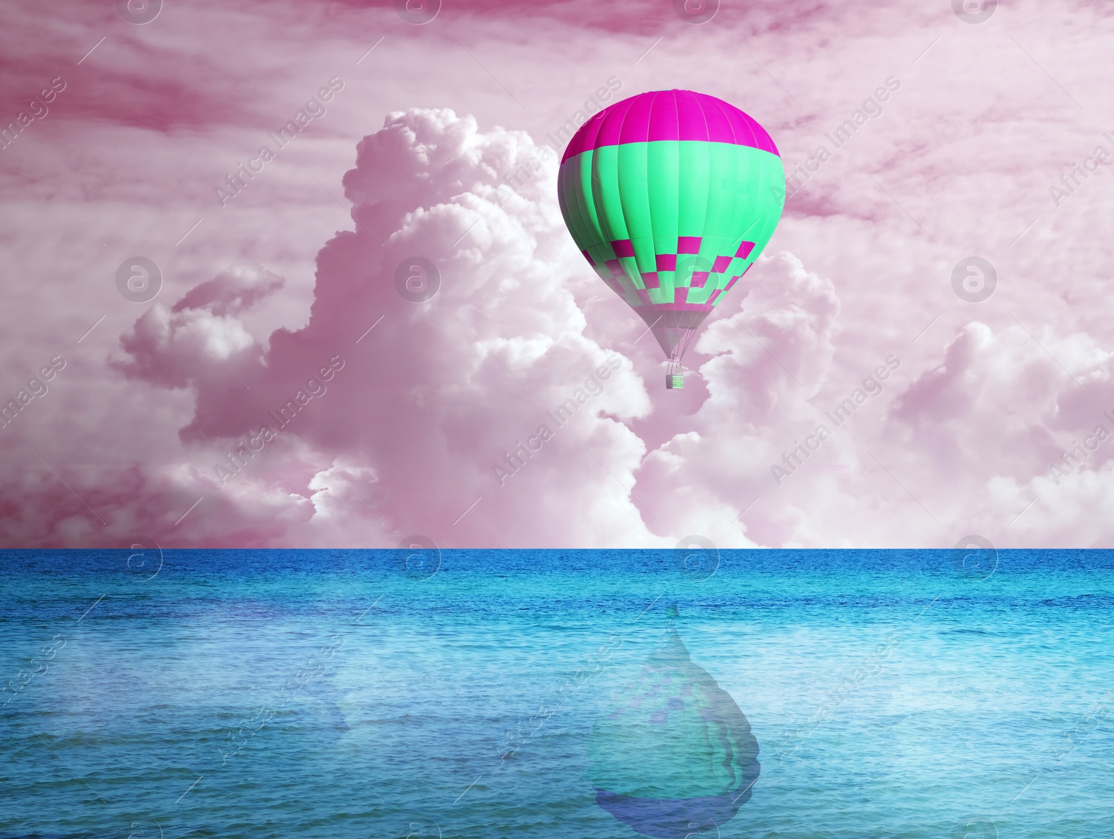 Image of Dream world. Hot air balloon in pink cloudy sky over blue sea