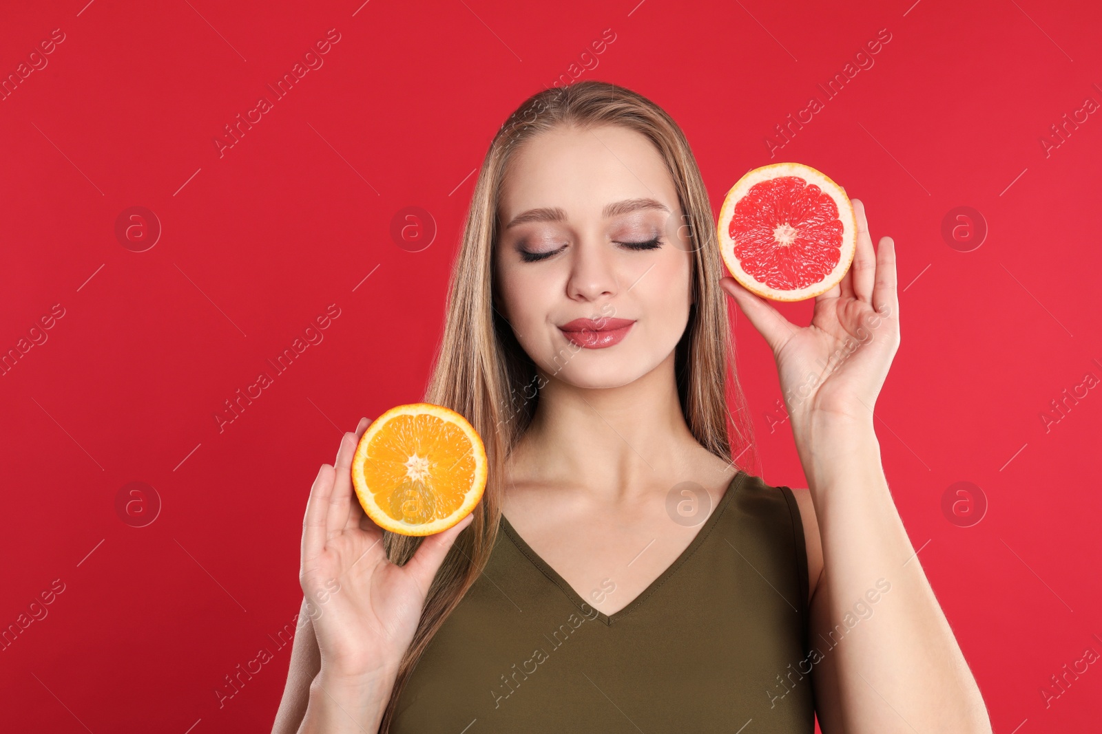 Photo of Young woman with cut orange and grapefruit on red background. Vitamin rich food