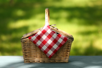 Wicker basket with blanket on table in park. Summer picnic