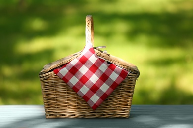 Photo of Wicker basket with blanket on table in park. Summer picnic