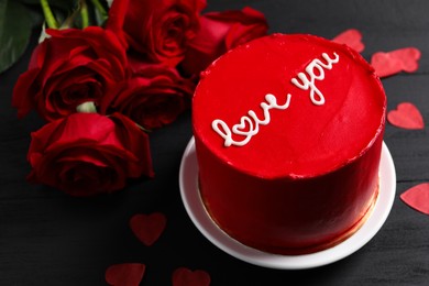 Photo of Bento cake with text Love You, roses and paper hearts on black wooden table. St. Valentine's day surprise