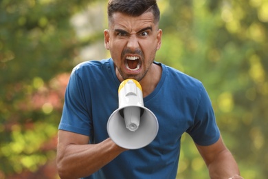 Angry young man with megaphone outdoors. Protest leader