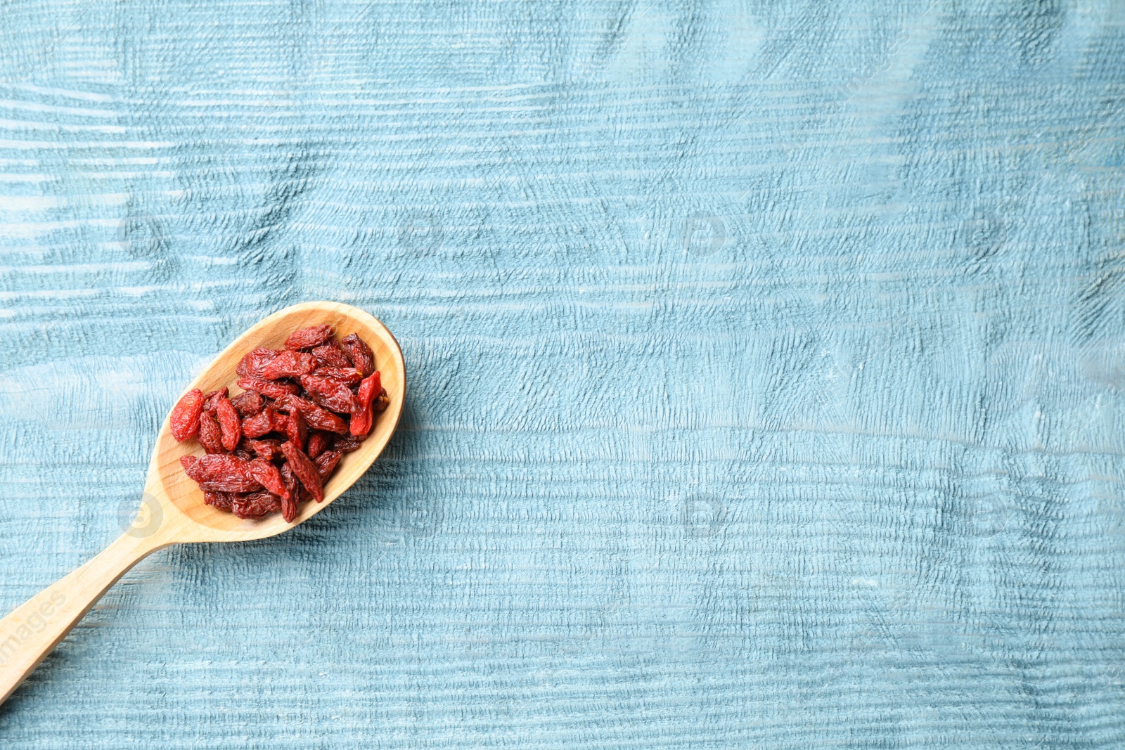 Photo of Dried goji berries on blue wooden table, top view. Space for text