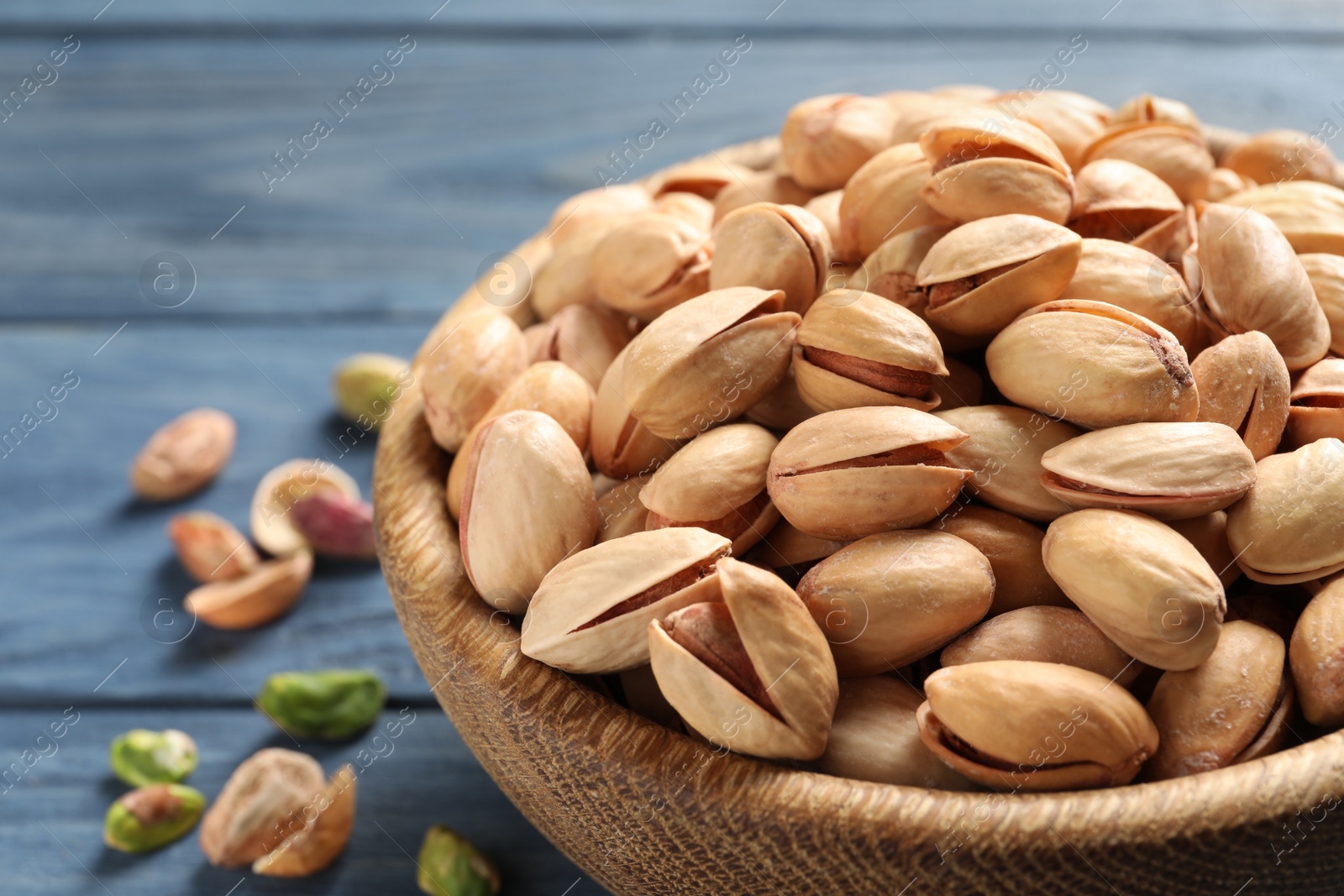 Photo of Organic pistachio nuts in bowl on wooden table, closeup