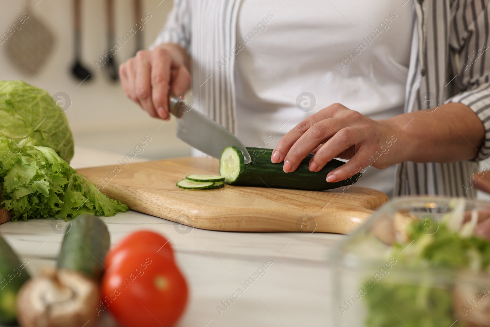 Photo of Woman cutting cucumber at white marble table, closeup