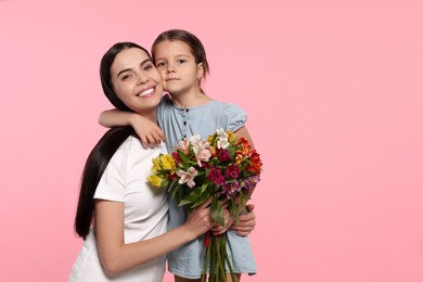 Happy woman with her daughter and bouquet of flowers on pink background, space for text. Mother's day celebration