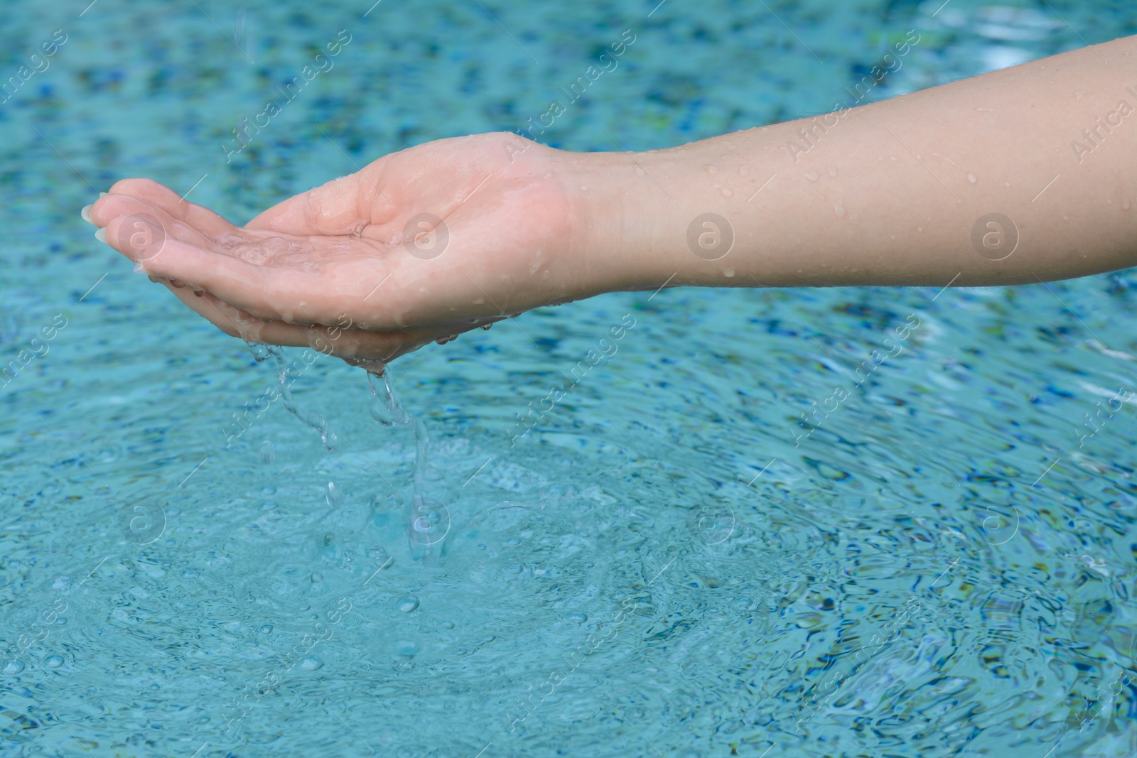 Photo of Girl holding water in hand above pool, closeup