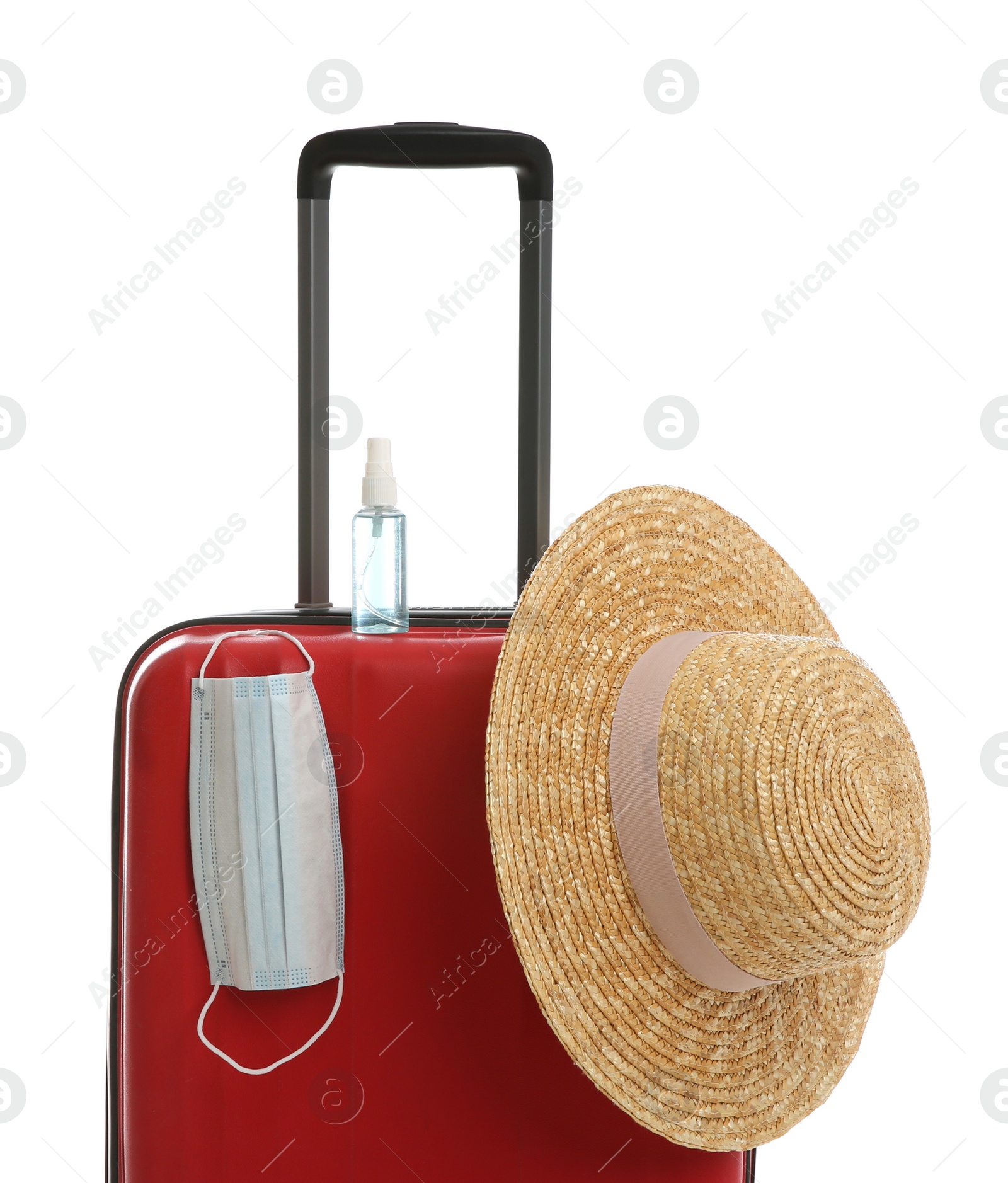 Photo of Stylish red suitcase with hat, antiseptic spray and protective mask on white background. Travelling during coronavirus pandemic