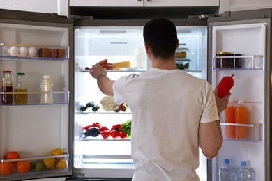 Photo of Man near refrigerator in kitchen, back view