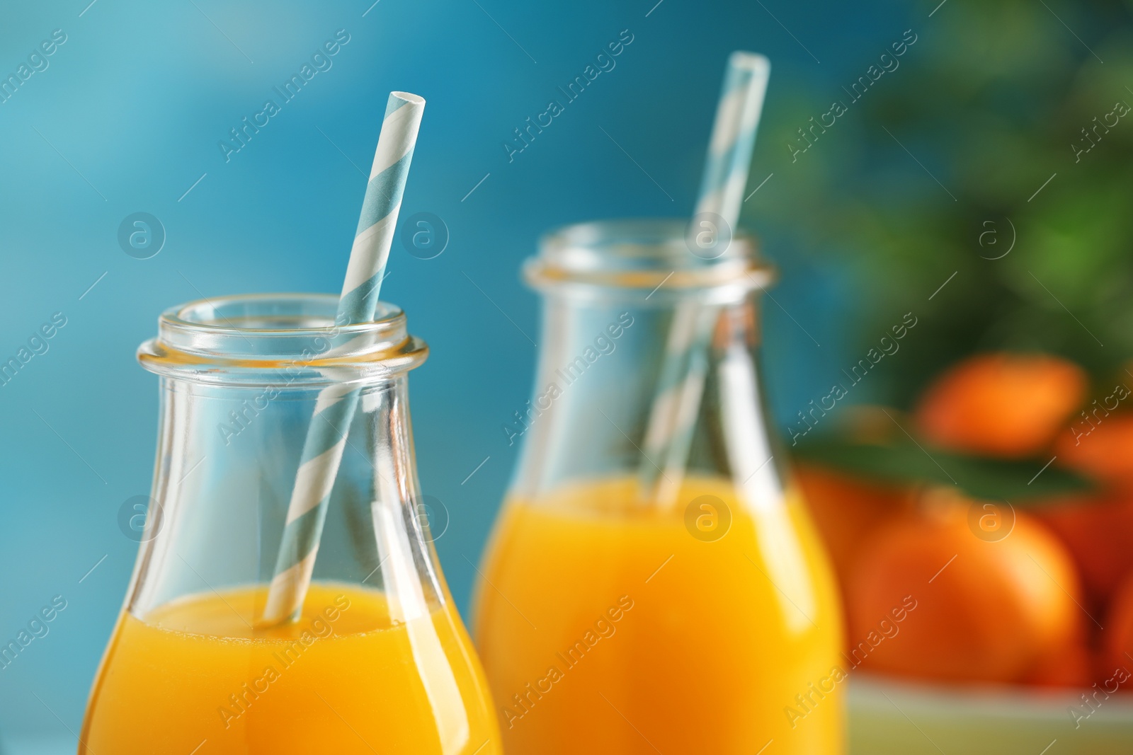 Photo of Bottles of fresh tangerine juice on blue background, closeup